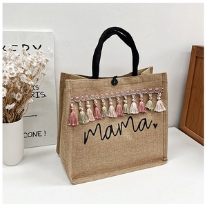 Detail shot of a linen tote bag featuring boho colorful tassels and black mama print decoration