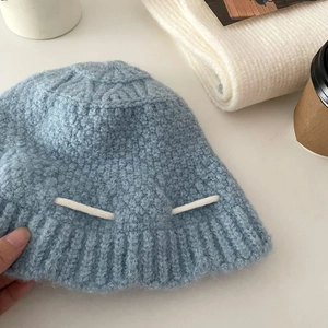 Close-up of blue knitted bucket hat featuring white rope detailing on a white surface