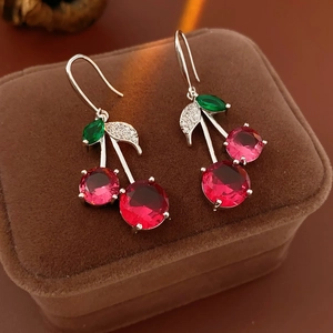 Macro shot of cherry-shaped earrings with red faceted gemstones and green zircon leaves