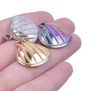 Close-up of shell-shaped pendants in silver, gold, and rainbow finish on a hand
