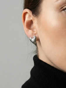 Detailed close-up of textured heart stud earring in silver finish worn by a model