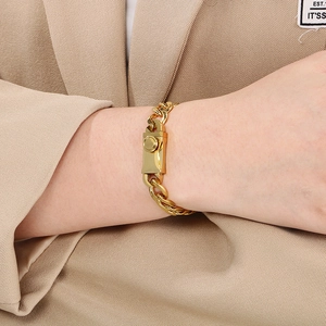 Close-up of a gold Figaro link chain bracelet with a square buckle on a model's wrist