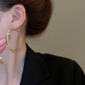 Gros plan de créoles dorées avec petits cristaux portées par un mannequin chic