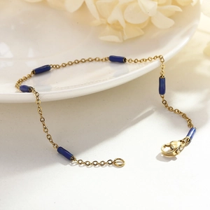 Détail d'un bracelet chaîne en perles de riz dorées avec accents en émail bleu sur plat blanc