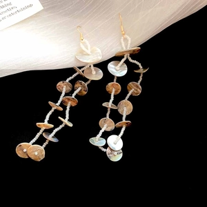 Detail of bohemian tassel earrings with iridescent shell discs and white beaded strands