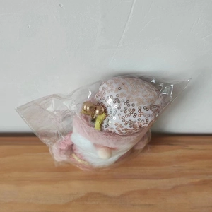 Detail view of a pink plush Christmas gnome with gold sequins in protective packaging
