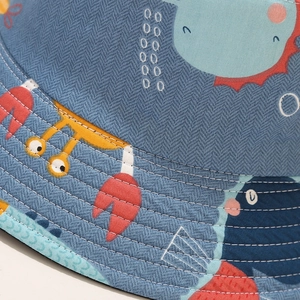 Detail of shark and crab pattern on denim blue bucket hat with white stitching