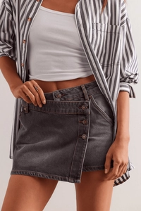 Détail d'une jupe en jean gris foncé avec braguette boutonnée asymétrique et boutons métal