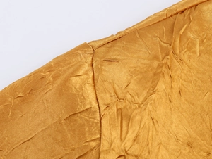 Macro-detail van gouden satijnen stof met elegante plooistructuur en fijn naaiwerk