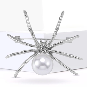 Silver spider brooch with white pearl and rhinestone accents on a minimalist background