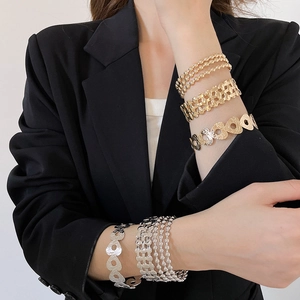 Close-up of gold layered metal bracelets with hollow heart and woven design on wrist