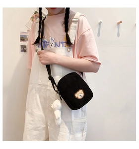 Detail of black corduroy shoulder bag with cute white plush bear charm on a model