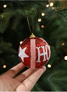 Close-up of red glitter Christmas ball with HO lettering and stars hanging on a festive tree