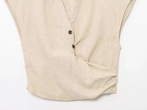 Dettaglio del top beige senza maniche in lino con bottoni e nodo intrecciato sul davanti