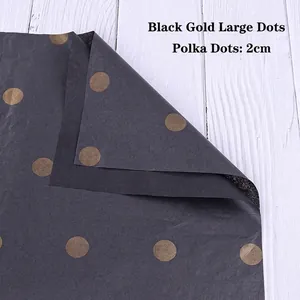 Detail of black floral wrapping paper with 2cm gold polka dots on white wood background