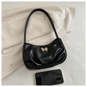 Detail of black pleated underarm bag with silver butterfly charm on beige suit