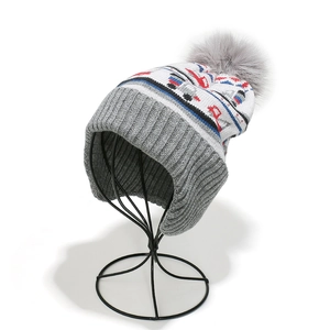 Detail of children's knit hat featuring cartoon construction vehicle patterns and a grey pom-pom