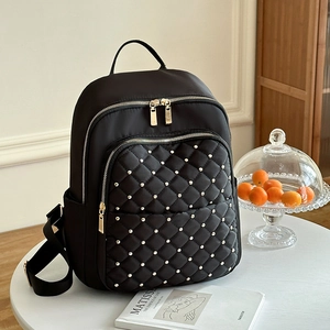 Zaino in nylon nero con trapuntatura a rombi e rivetti dorati su un tavolo bianco