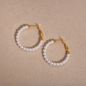 Detailed close-up of C-shaped gold hoop earrings with polished white pearls