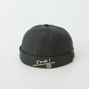 Detailed close-up of the I'm OK smiley face embroidery and CUTE red label on black skull cap