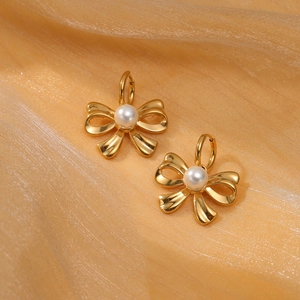 Elegant gold bow earrings with pearl center on golden silk fabric background