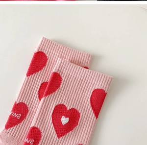 Close-up of pink knit socks featuring red heart patterns with white Love text embroidery