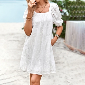 Elegante abito corto bianco con scollo quadrato, ricamo e maniche a sbuffo sulla spiaggia