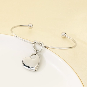 Detail of silver stainless steel open bangle with heart charm on ceramic plate