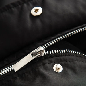 Macro detail of the silver metal zipper and snap button on black bomber jacket fabric
