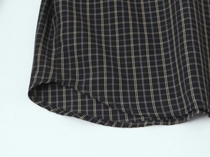 Detail of dark grey plaid cotton shirt showing curved hem and double stitching