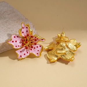 Golden flower earrings with pink enamel petals and red dots on warm yellow background