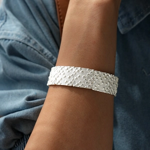 Détail d'un large bracelet en métal martelé argenté sur fond de denim bleu