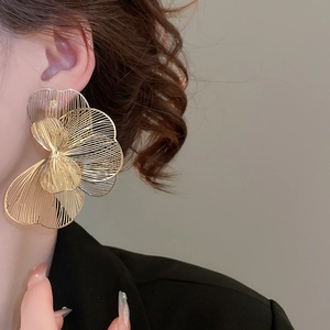 Gros plan de boucles d'oreilles fleurs dorées ajourées avec texture de pétale brossé