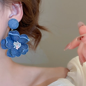 Macro detail of denim fabric floral earrings featuring pearl stamen and frayed edges