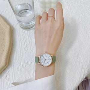 Dettaglio del cinturino in pelle verde e orologio al quarzo dorato con quadrante bianco al polso