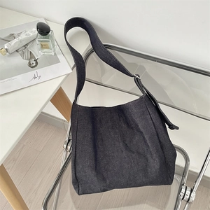 Detail of blue denim hobo bag on a chair showing the wide strap and silver metal buckle