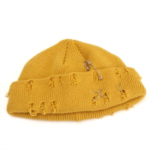 Detail of yellow knit beanie featuring distressed holes and metal ring pin decorations