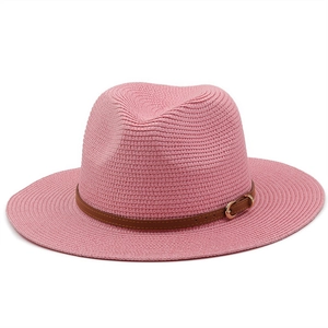 Detail of pink straw sun hat featuring a brown leather band and gold buckle accent