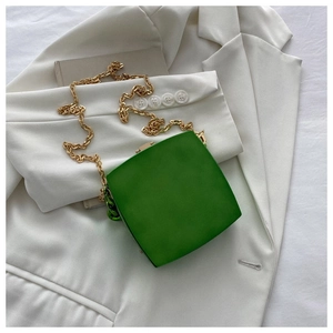 Detail view of a green box bag with gold chunky chain placed on a white blazer