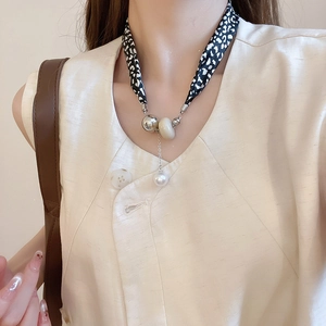 Détail du collier en tissu léopard avec perles métalliques et un pendentif perle