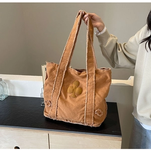 Detail of caramel canvas tote bag featuring raw frayed edges and a plum blossom patch