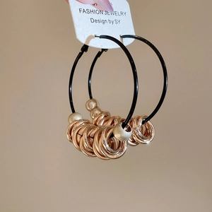 Detail view of black cord hoop earrings with layered gold small ring charms held by hand