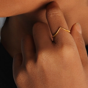 Close-up of minimalist golden V-shaped ring worn on finger showing fine metal texture