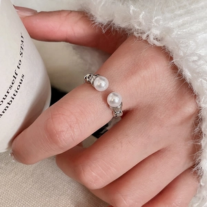 Detail of silver open ring with double white pearls on model hand with soft background