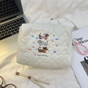 Close-up of heart-quilted cream makeup bag with dog embroidery and pink wrist strap