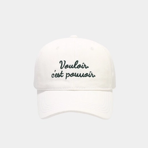 Close-up of white cotton baseball cap featuring green Vouloir c'est pouvoir embroidery