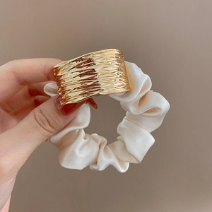 Detail of a beige satin scrunchie featuring a polished gold geometric metal buckle
