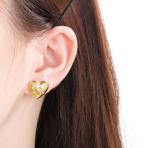 Close-up of heart-shaped gold stud earrings with diamond accents and quilted pattern