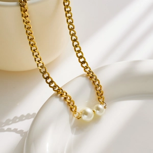 Close-up of golden Cuban chain necklace featuring two cream white pearls on white ceramic