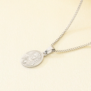 Detail of silver oval Virgin Mary pendant with box chain on a textured surface